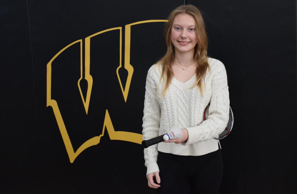 student holding badminton racket in front of yellow W